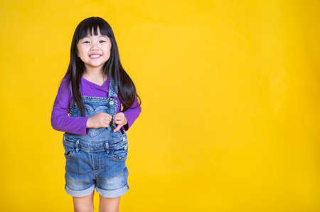 Portrait of young happy little asian girl in uniform isolated on yellow background with copy space....