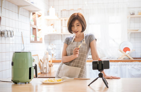 Portrait of beauty asian woman review cooking fry potato food , recording live video using air flyer smart device at home. Online influencer girl on social media marketing, hobby and leisure conceptの写真素材