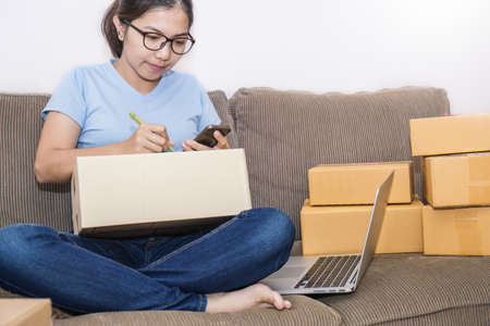 Start up small business entrepreneur SME freelance woman working at home office concept, Young Asian small business owner using smartphone, online marketing packaging and delivery, SME conceptの写真素材