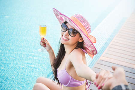 Beautiful asian female model drinking cocktail holding hand glass posing by the pool, outdoor portrait banner. Beach asian woman having fun in summer vacation holidays. Girl in tropical summer weatherの写真素材
