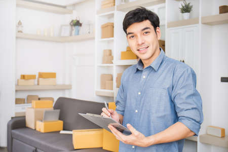 Startup small business entrepreneur SME, asian man writing on clipboard. Portrait young Asian small...