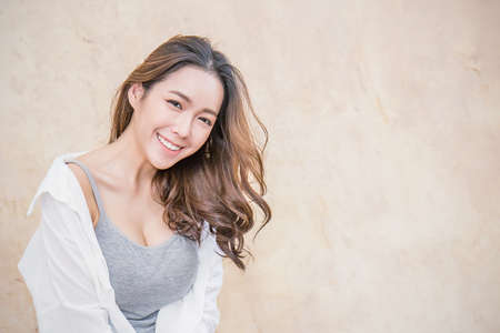 Portrait of young beautiful asian woman sit and relax over vintage wall. Smile happy asian girl...
