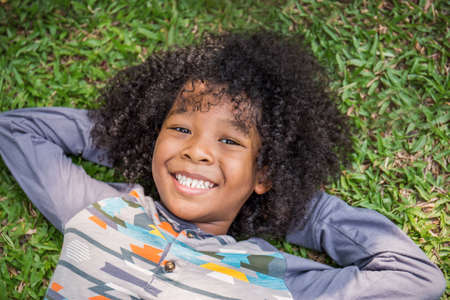 Close up portrait of young little black boy lying having good time in the park(green grass). Fun in the park childhood spring or summer time concept.の写真素材