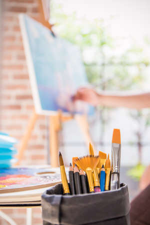Close up paint brush in art studio with background of oil painting canvas. Art class workshop painting education concept.の写真素材