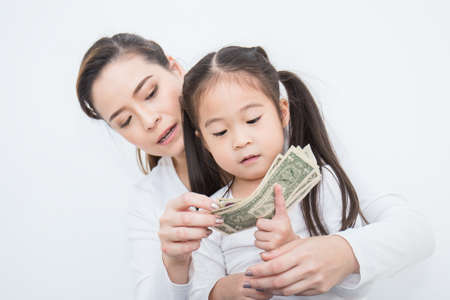 Portrait of cute little asian girl and mother holding money isolated on white background. Small asian girl counting her allowance dollar note.の写真素材