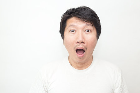 Attractive surprise asian man. Closeup portrait asian man wearing t-shirt isolated on white background. Expression emotion shock surprise concept.の写真素材