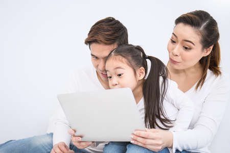Portrait Asian family looking at a tablet computer while lying on the bed, little asian girl using laptop with her parents. Weekend holiday leisure time education e-commerce online shopping telemarketing technology conceptの写真素材