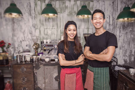Startup successful small business owner man and woman standing with arms crossed in his coffee shop or restaurant. Portrait of young asian tan couple barista cafe owner. Small business entrepreneur together teamwork concept.の写真素材