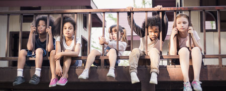 Multicultural little children sitting behind the fence. Homeless orphan stressful kids, education human right day concept bannerの写真素材