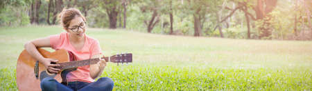 Pretty asian young girl playing some record on guitar in the park. Asian woman hands playing...