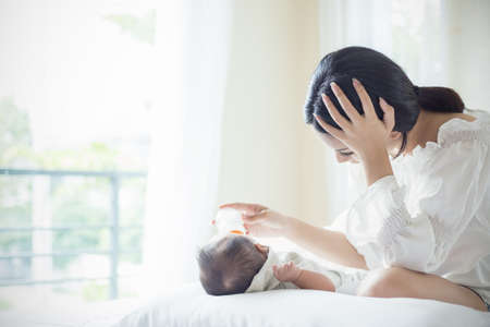 Asian Mother nursery feeding bottle of formula milk to newborn baby in bed suffering from post natal depression. Health care single mom motherhood stressful concept.の写真素材