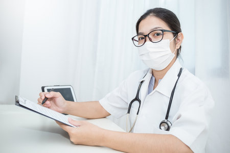 Closeup portrait of Asian doctor woman with hand holding pen examining checking checkup list paper . Healthcare and medical sickness conceptの写真素材
