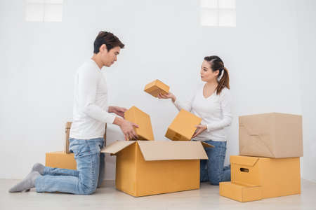 Asian woman and asian man carry boxes sitting on the floor with pile of boxes. Moving to new house...