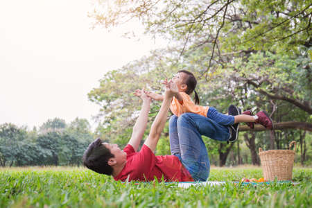 Happy asian father and daughter playing in the park. Asian man and little toddler girl lying hugging in the park. Happy family green spring or summer fatherâs day together conceptの写真素材