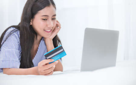 Portrait of beauty asian girl or woman on bed using computer laptop  shopping online with credit...