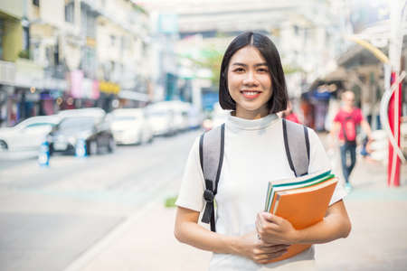 Smiling young asian woman with her book backpack in the city. Portrait of beautiful asian girl walking to school. Education tutor authentic lifestyle people back to school conceptの写真素材