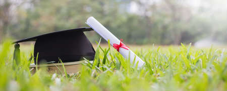 Closeup certificate paper and black cap on green grass spring time in the outdoor park. Education happy success achievement graduated celebrate graduate day concept panoramic background bannerの写真素材