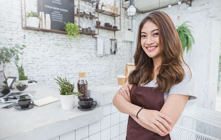 Startup successful small business owner beauty girl standing with arms crossed in coffee shop or restaurant. Portrait of young asian tan woman barista cafe owner. SME entrepreneur business conceptの写真素材