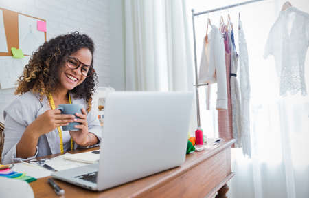 Portrait of beautiful smile african american black designer woman work with computer in tailer fabric fashion small business workshop office. Young owner entrepreneur creative girl textile business conceptの写真素材