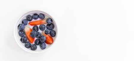 Close up bowl of fresh mixed berries and yogurt with farm fresh strawberries on white table background. Health care organic food vegan vegetarian breakfast modern lifestyle concept bannerの写真素材