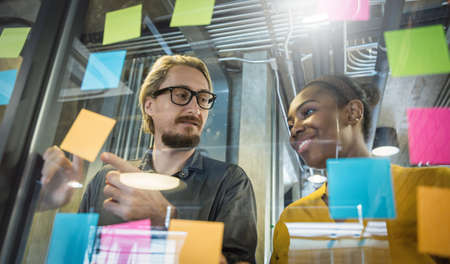 Portrait of business creative people man woman meeting at office and use sticky notes to share ideas. Brainstorming together teamwork synergy acquisition concept.  Coworker writing in note pad on the wall.の写真素材