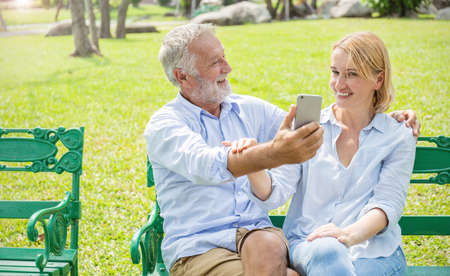 Senior caucasian couple take a self portrait together with smartphone. Closeup old mature man and woman selfie at the park. People lover lifestyle technology connection social online network virtualの写真素材