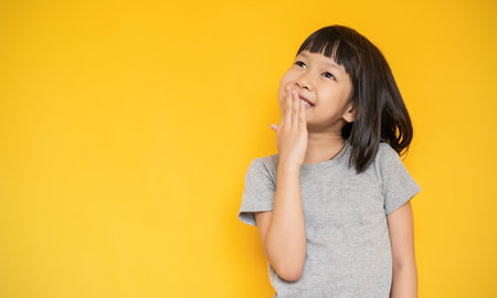 Portrait of young beautiful little asian girl looking isolated on yellow background wall with copy...