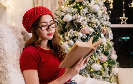 Portrait of nerd asian woman hold book in winter Christmas living room. Smile happy asian girl  knowledge education university woman asia winter lifestyle, back to school.の写真素材