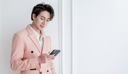Portrait of Korean asian handsome smile friendly Business model man in pink suit text on smart phone, business man smart with success, executive with leadership, office fashion workspace technology.の写真素材