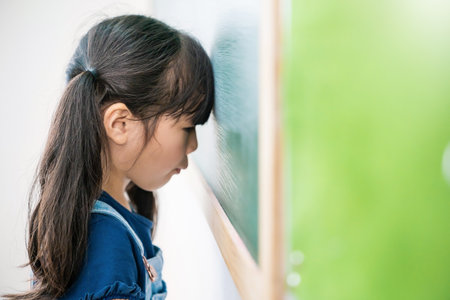 Portrait of sad little asian girl lean head near the blackboard indoors. Kid is learning in class...