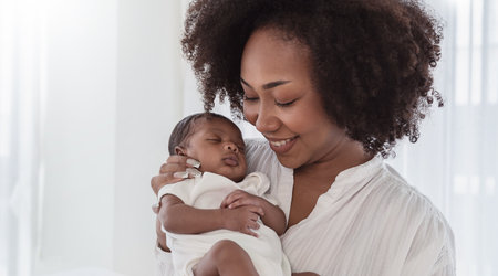 Close up portrait of beautiful young African American  mother holding sleep newborn baby in hospital bed room. Healthcare medical love black afro woman lifestyle mother's day, breast with copy space.の写真素材