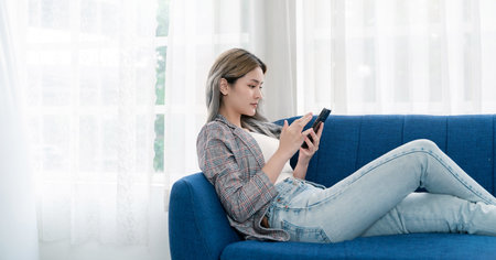 Portrait of young beautiful asian woman relax use smartphone gadget on sofa. Smile happy asian girl online shopping work from home. Education e-commerce freelance technology sme connected asia peopleの写真素材