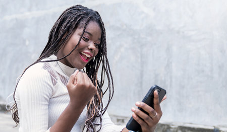 Portrait of beautiful African American successful business girl celebrate with smartphone with copy space on street background. Success  happy woman education internet technology startup business.の写真素材