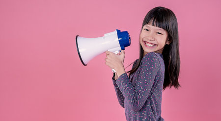 Portrait of young fun smart happy little asian long hair girl isolated on pink studio shot. Education for elementary kindergarten, little girl hold megaphone loudspeaker back to school concept.の写真素材
