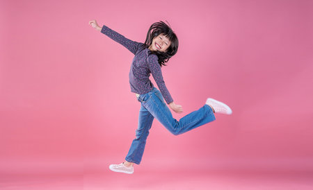 Portrait of young fun smart happy little asian jump and dance on pink background studio shot....
