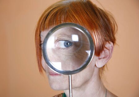 Red haired woman with blue eye peering through a magnifying glassの写真素材