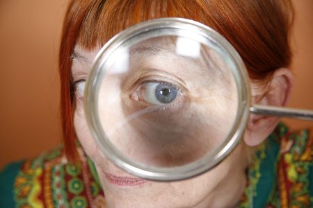 Red haired woman with blue eye peering through a magnifying glassの写真素材