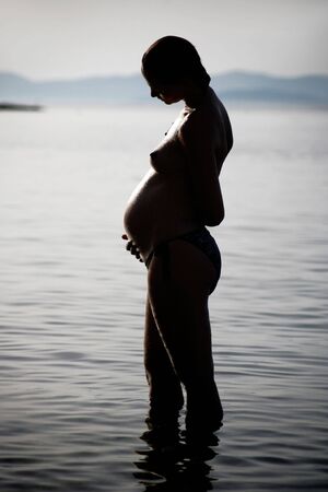 Young pregnant woman standing in sea holding tummyの写真素材