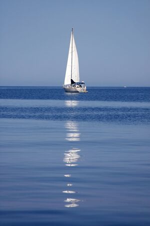Sailboat with white sail reflected in calm mediterranean waters, Croatiaの写真素材