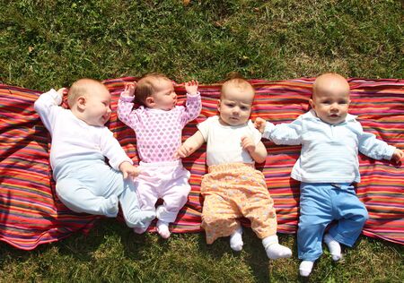 Four babies lying on colourful cloth in grass in parkの写真素材