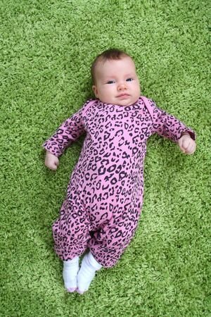baby laying on his back on green carpet in pink leopard outfitの写真素材