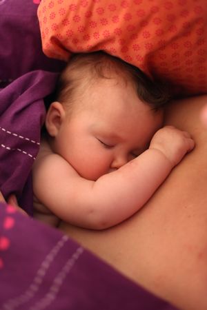 Young baby sleeping on mother in purple bed sheetsの写真素材