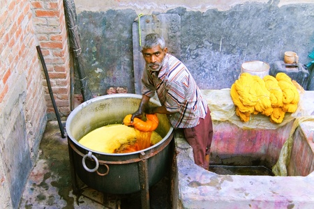 DELHI - DECEMBER 2: Worker dyeing fabric with pot of orange dye on December 2, 2007 in Delhi, India. Most traditional dyeing is done by hand.のeditorial素材