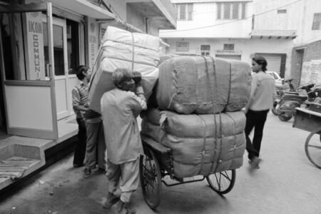 DELHI - DECEMBER 2 (shot in black and white): Adult man and boy lifting parcels onto trailer wagon on December 2, 2007 in Delhi, India. Most local transport is done by human effort.のeditorial素材