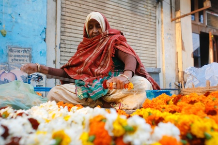 DELHI - JANUARY 19: Woman threading colourful flower garlands on January 19, 2008 in Delhi, India. These flowers are offered to the gods in the templesのeditorial素材