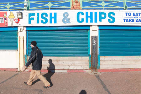 BRIGHTON, UK - FEBRUARY 8, 2011: Man walking in front of closed fish and chips shop on February 8, 2011 in Brighton, UK. Stores are closed over the winter there are few tourists.のeditorial素材