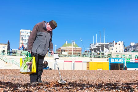 BRIGHTON, UK - FEBRUARY 8, 2011: Old man looking for metal objects on the beach with a metal detector on February 8, 2011 in Brighton, UK. There are an estimated 2 million pensioners living below the breadline.のeditorial素材