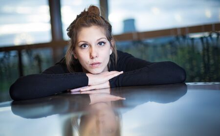 Beautiful woman looking intensely with chin on hands with slight reflection on tableの写真素材