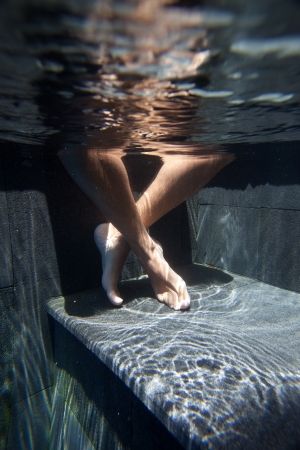 Crossed legged feet in pool with water ripple reflection on stepの写真素材