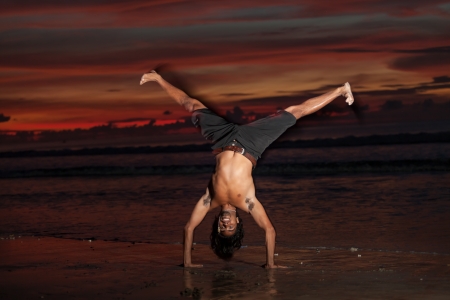 Young man doing capoeira on beach at sunsetの写真素材